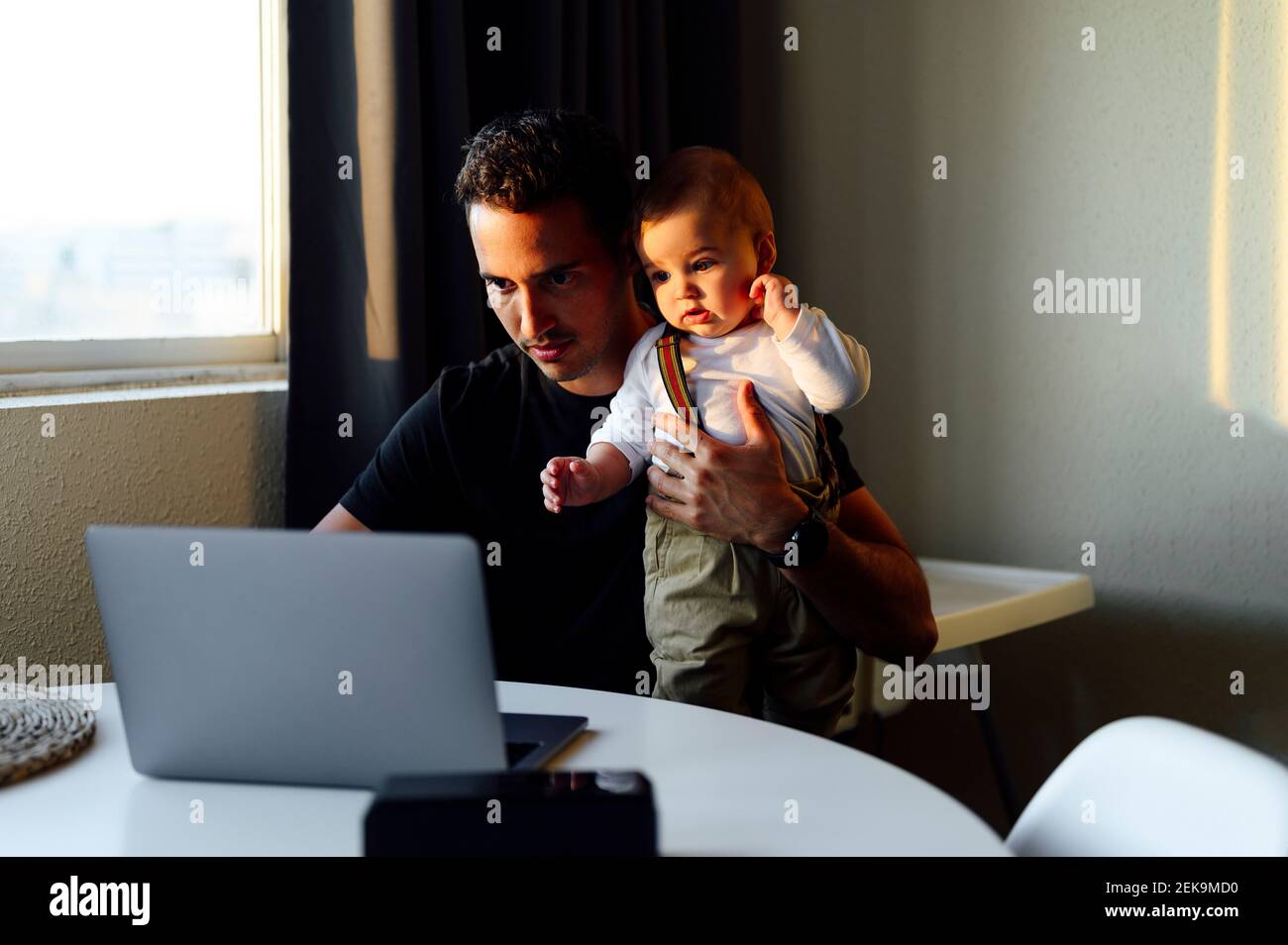 Father holding baby boy while working on laptop at home Stock Photo - Alamy