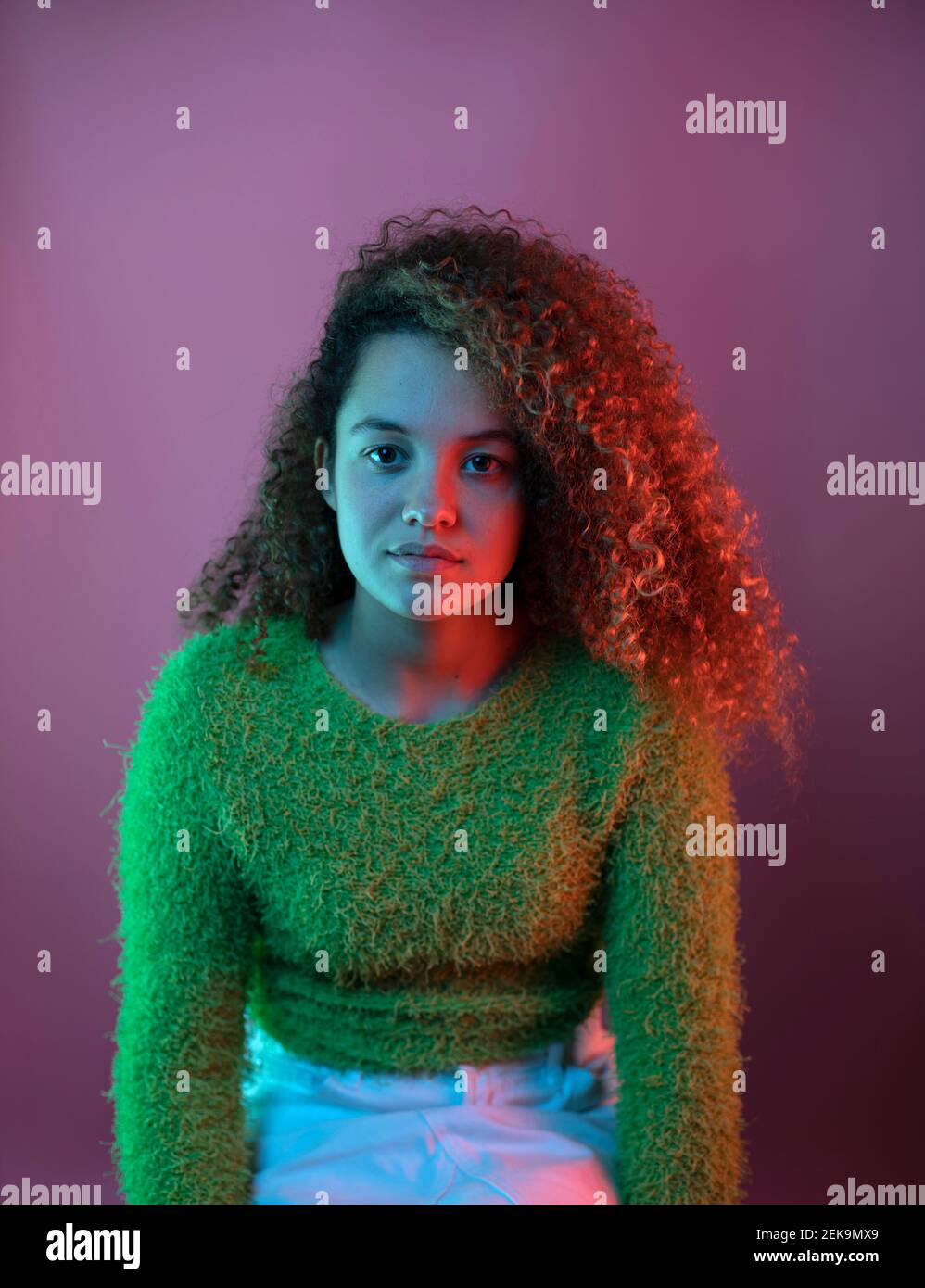 Red light on fashionable woman with curly hair sitting against pink background Stock Photo