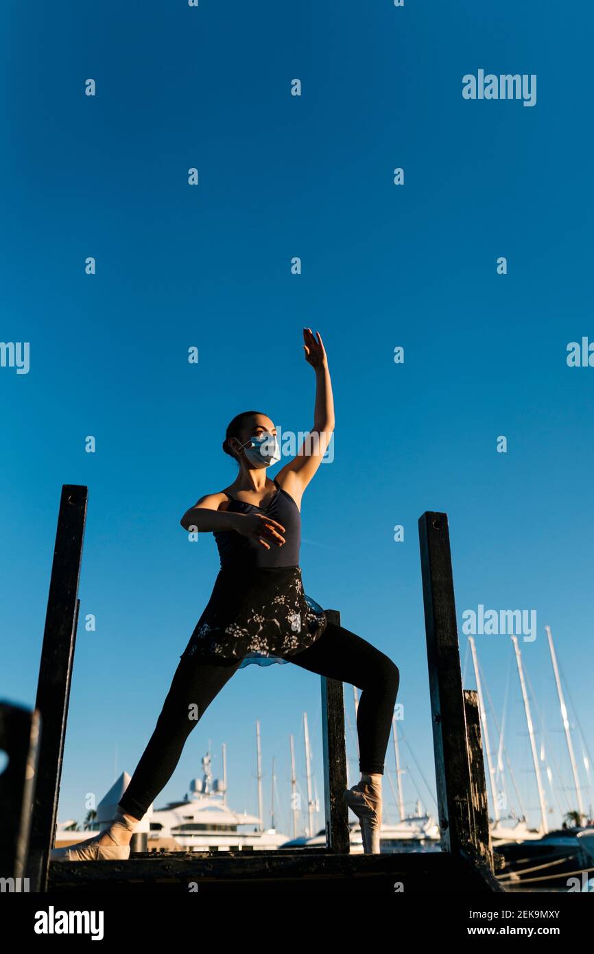 Young female ballet dancer practicing on jetty against blue sky Stock Photo