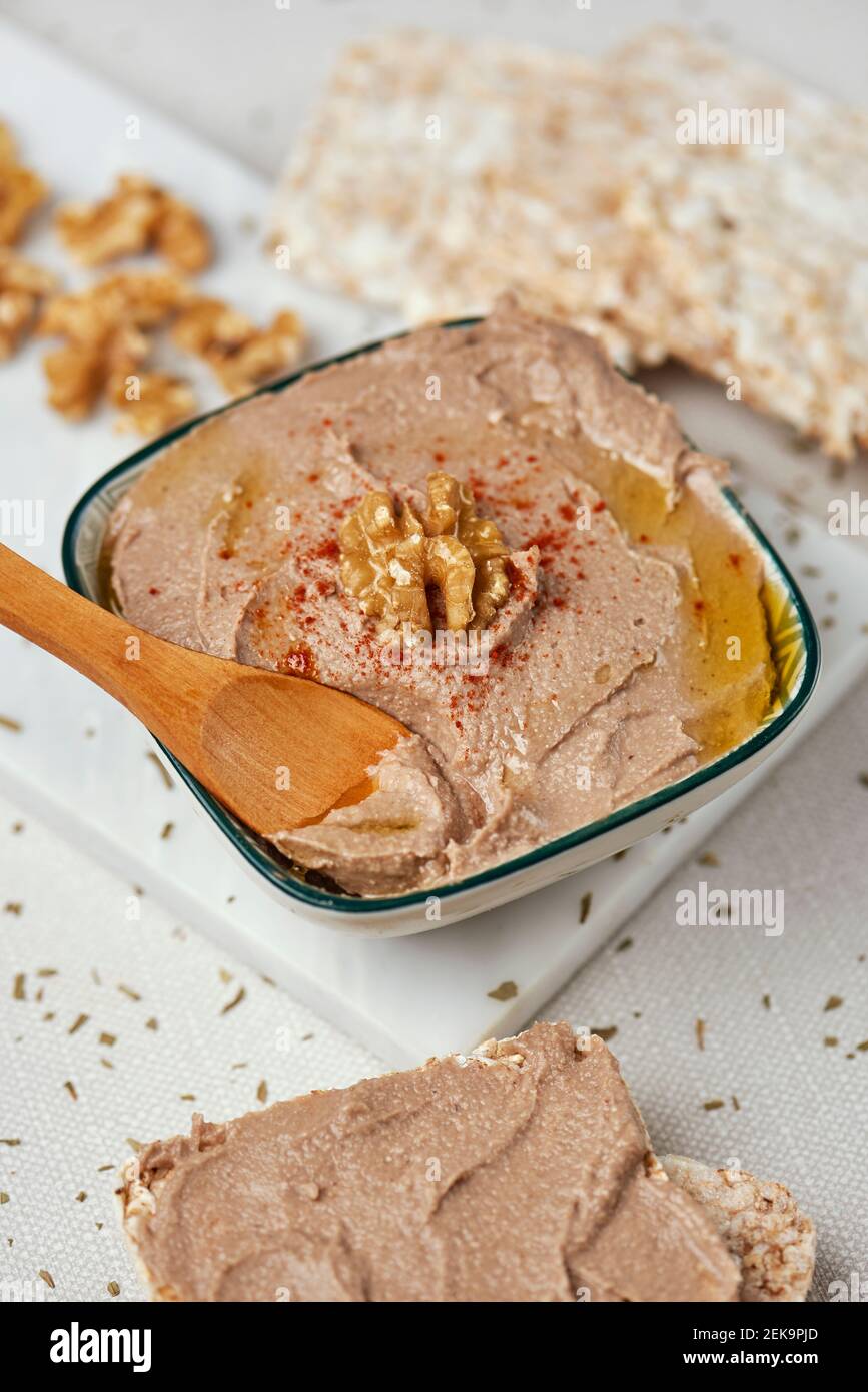 a rectangular ceramic bowl with an appetizing hummus, made with chickpea, walnut and rosemary, on a table, next to some puffed rice cakes Stock Photo