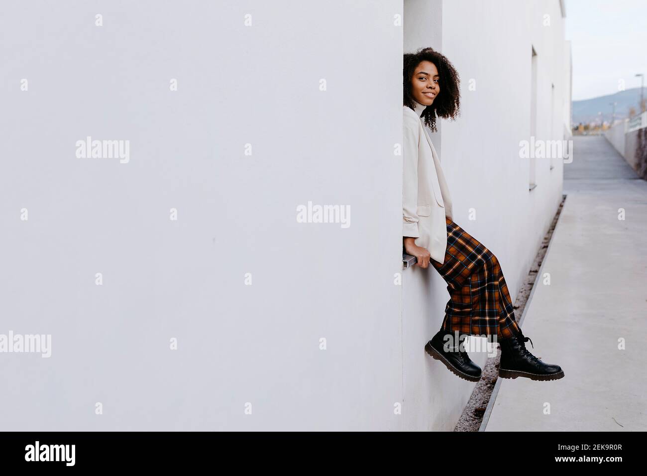 Young woman with afro hair sitting on window sill of white building ...