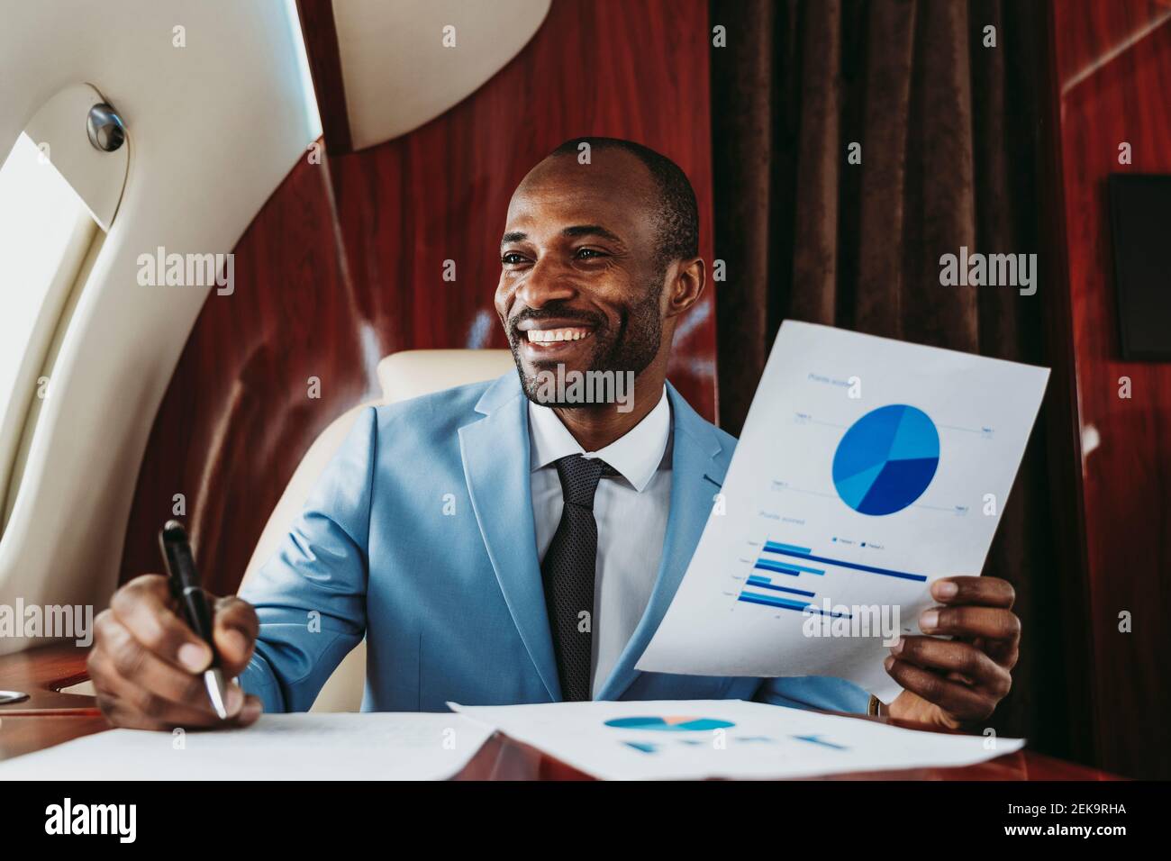 Smiling businessman looking away while holding pie chart in airplane Stock Photo