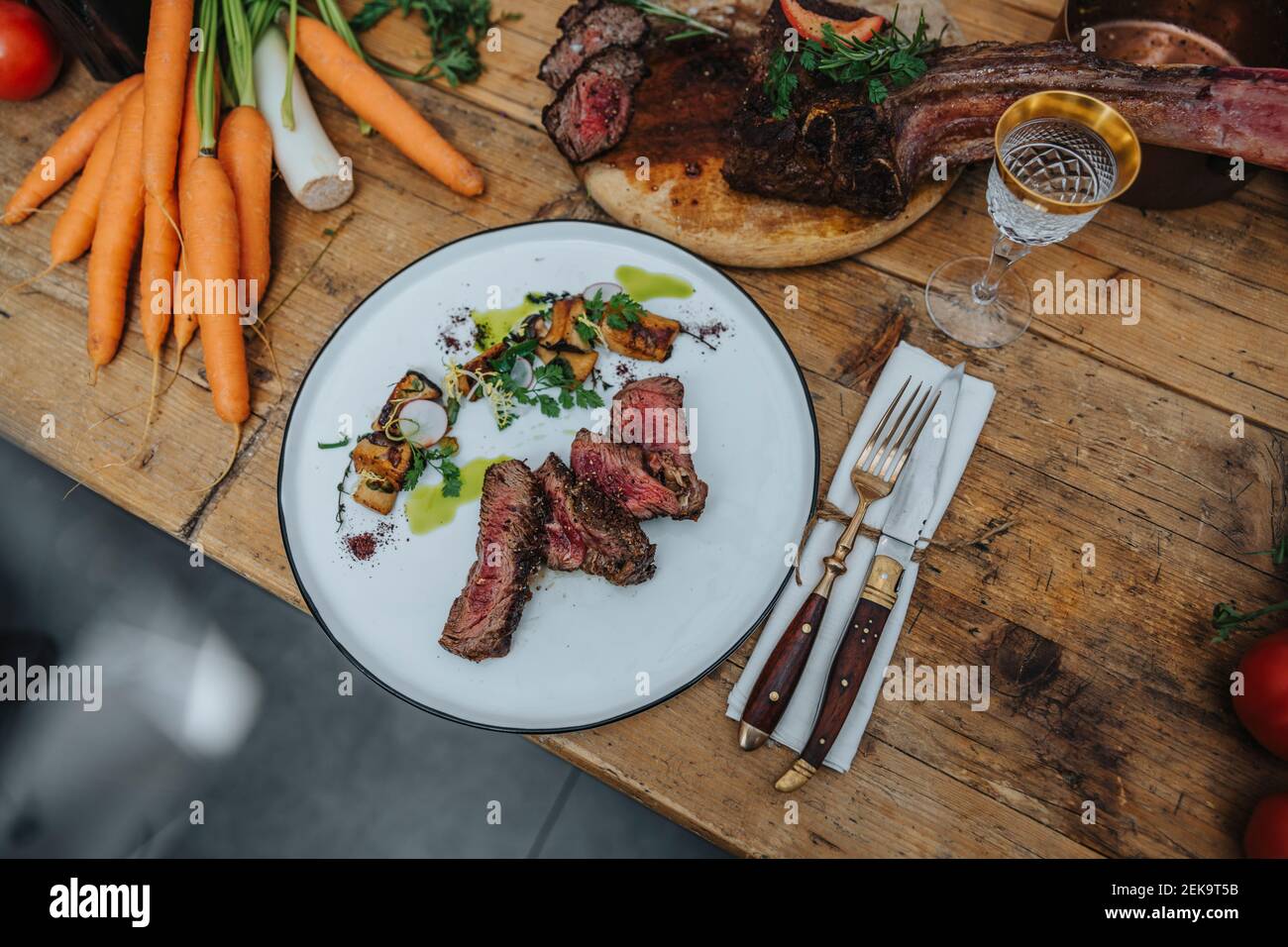 Tomahawk steak garnished with cooked vegetable in plate on kitchen island Stock Photo