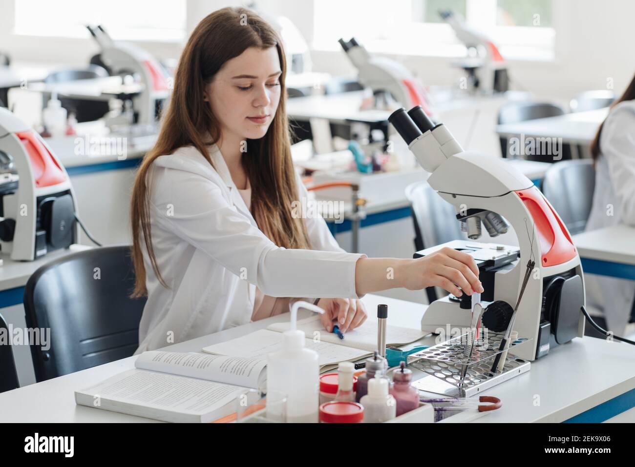 Young female researcher in white coat working in lab with a laboratory sample Stock Photo