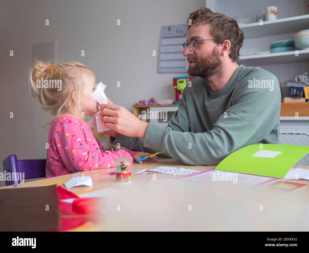 Playful father holding paper on daughter's while sitting at table Stock Photo