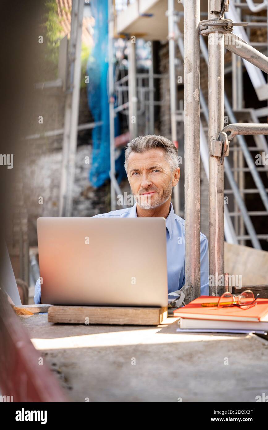 Smiling architect using laptop while sitting at construction site Stock Photo