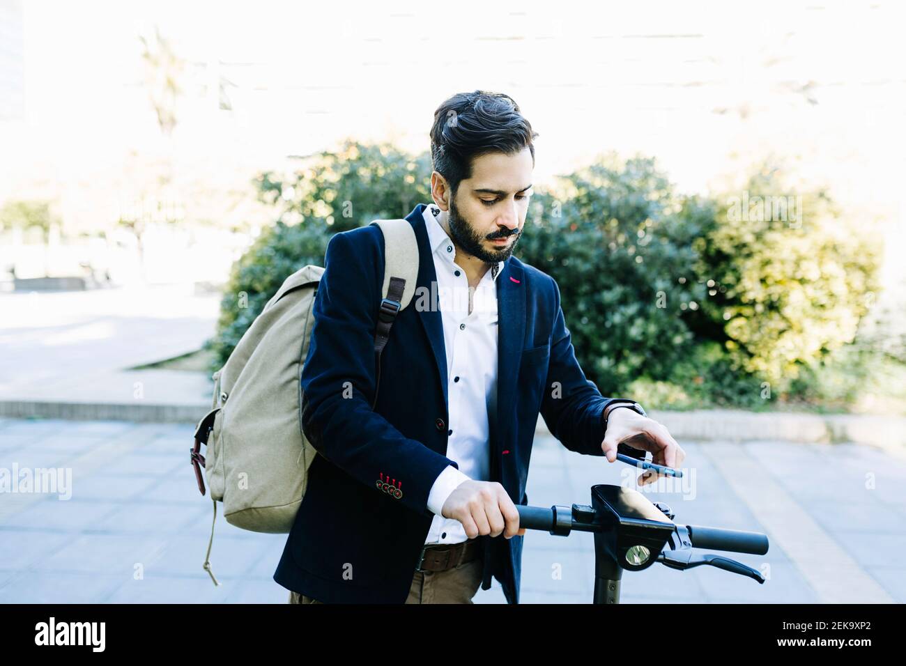 Mid adult businessman with backpack using mobile phone while standing by bicycle Stock Photo