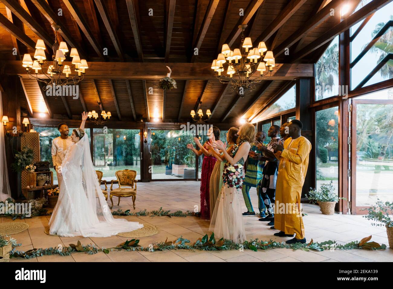 Bride throwing bouquet toward friends standing behind at banquet Stock