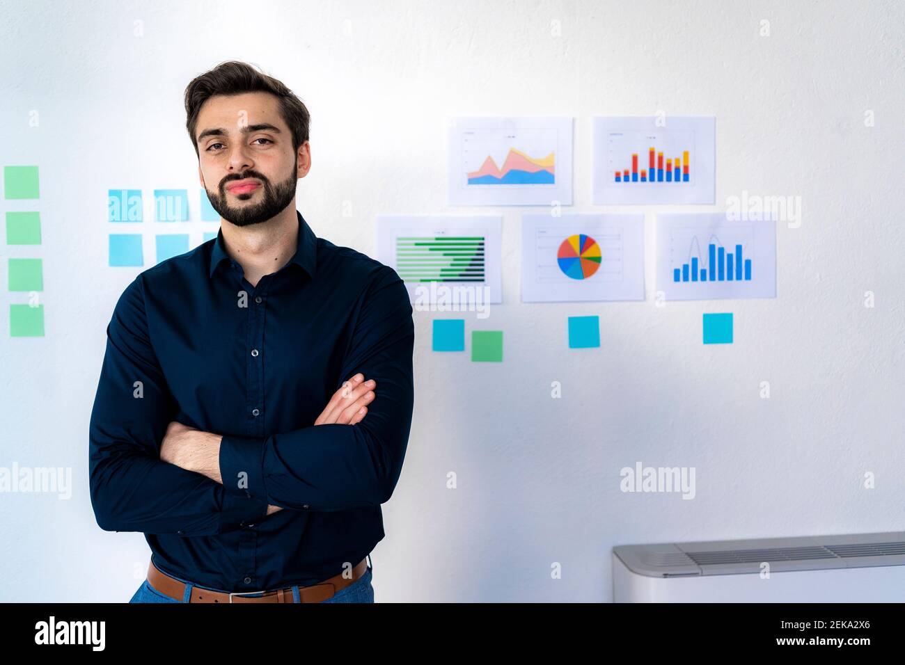 Confident male entrepreneur with arms crossed standing against wall in ...