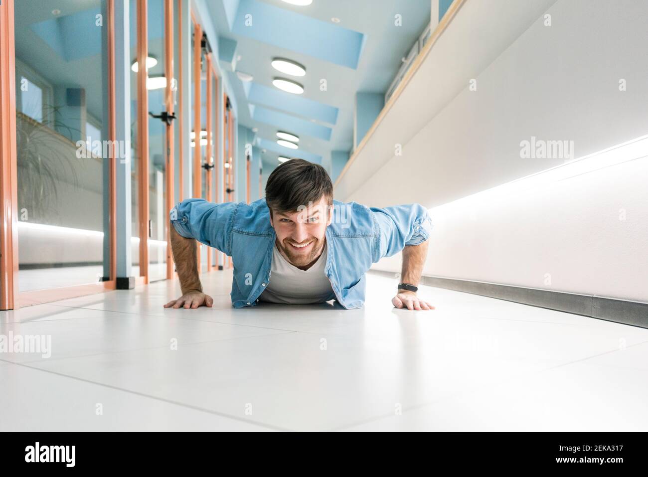 Smiling businessman doing push ups in office corridor Stock Photo