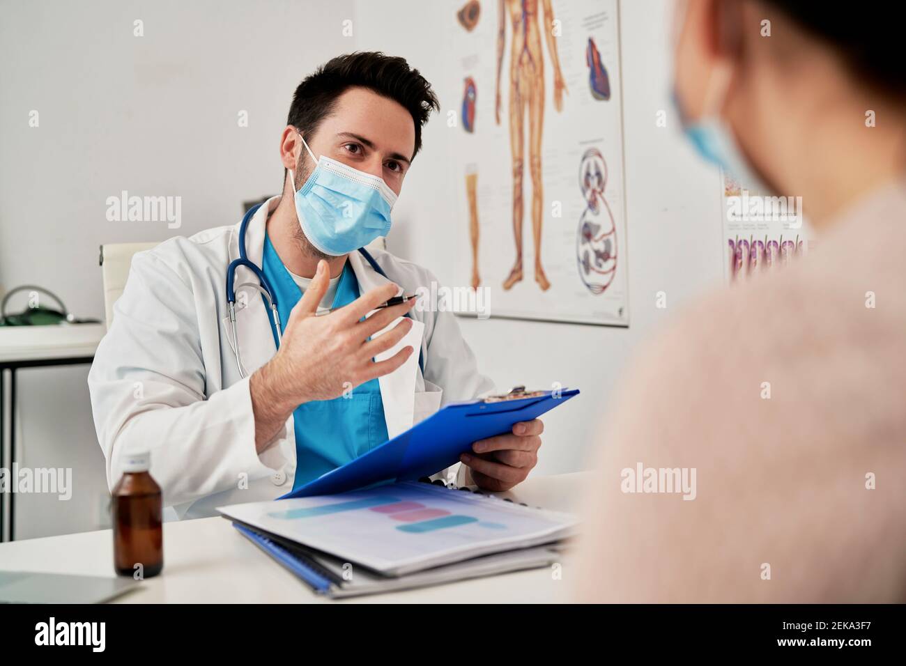 Male doctor with protective face mask talking with patient in clinic Stock Photo