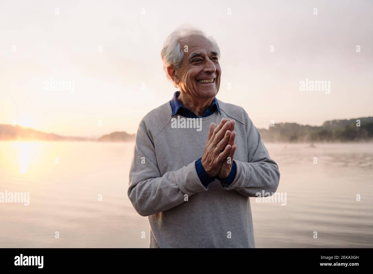 Smiling man standing with hands clasped against lake Stock Photo