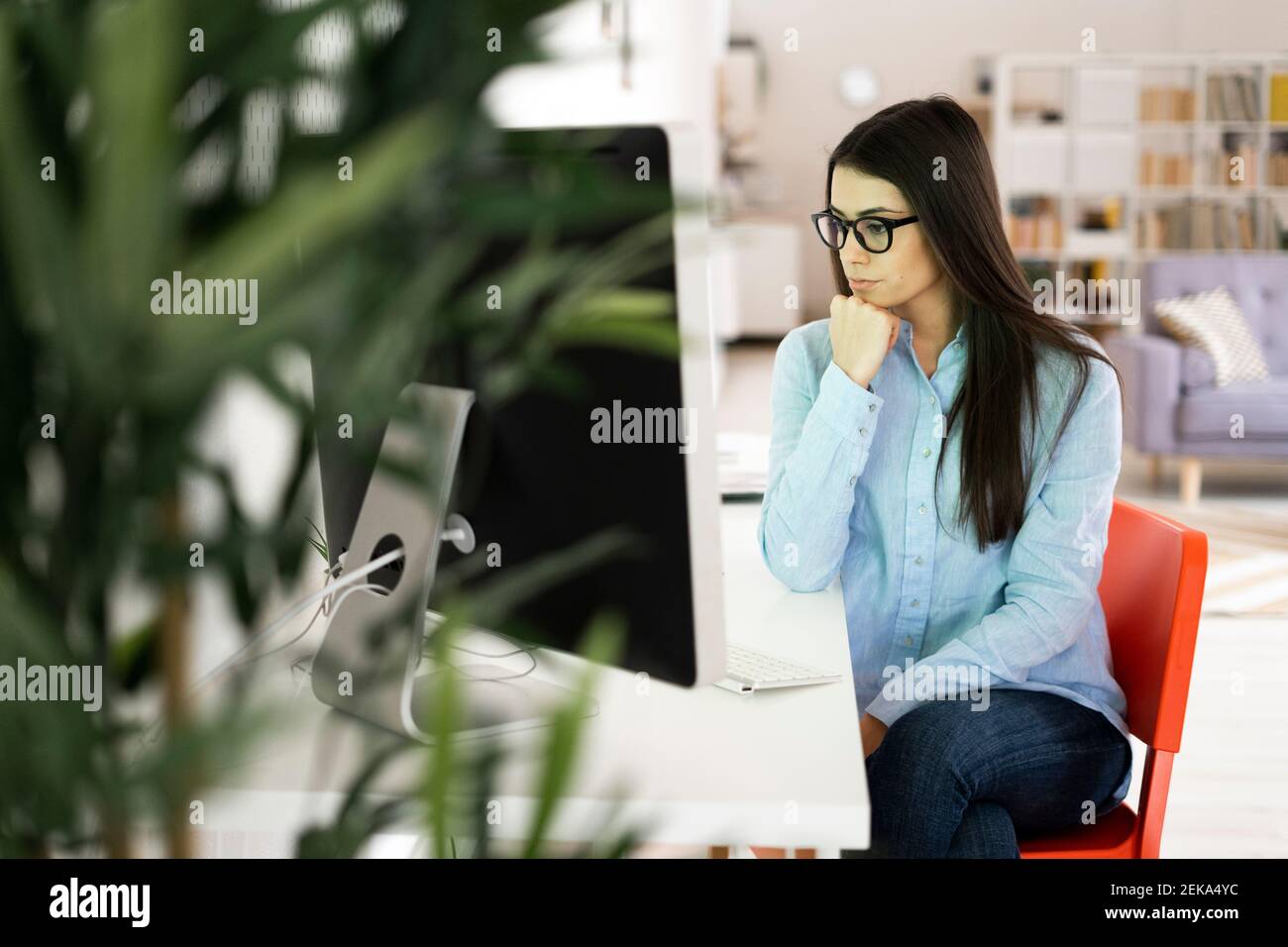 Thoughtful businesswoman with hand on chin looking away while sitting at office Stock Photo