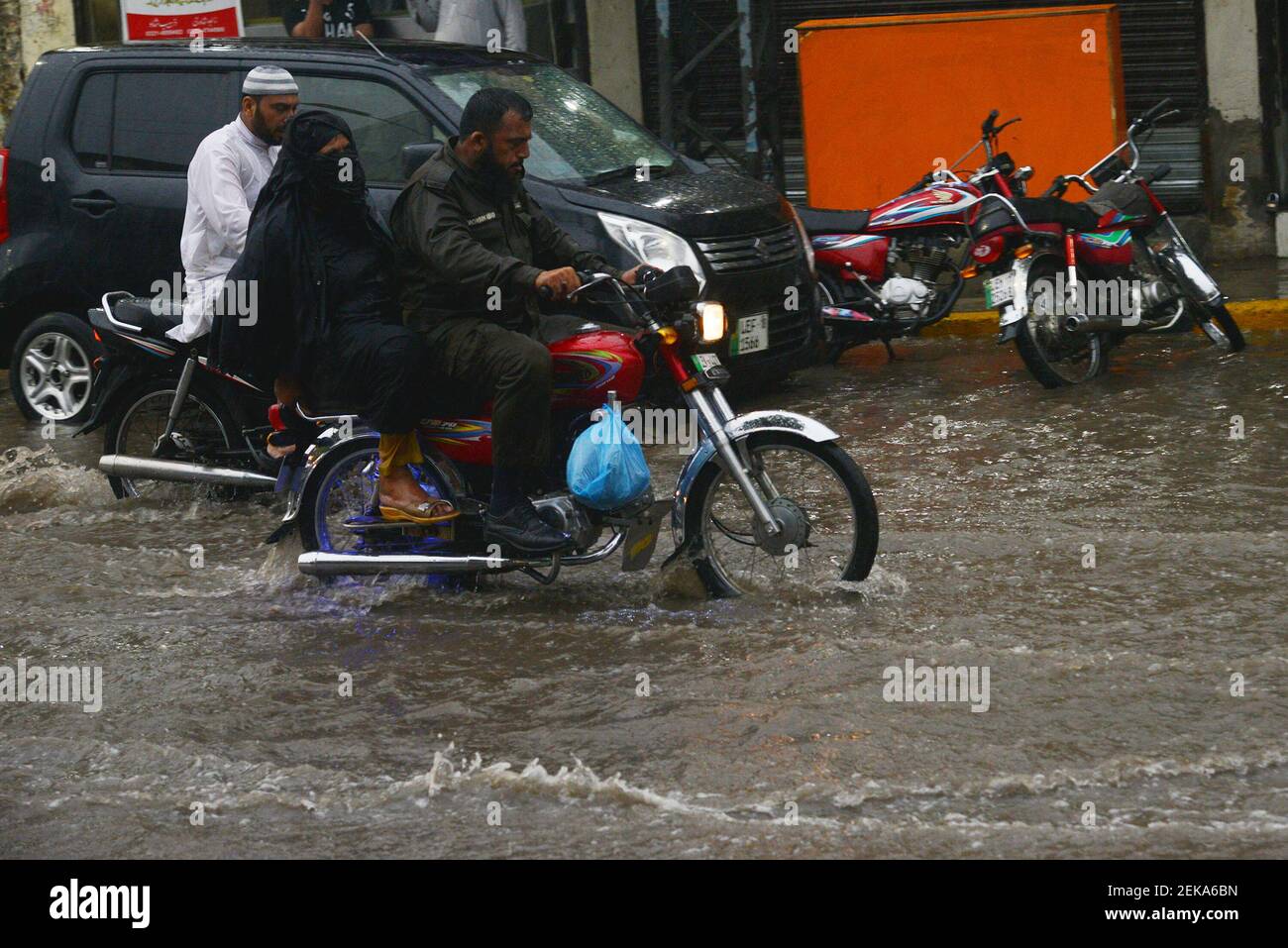 Pakistani commuters wade through a flooded street after heavy monsoon ...