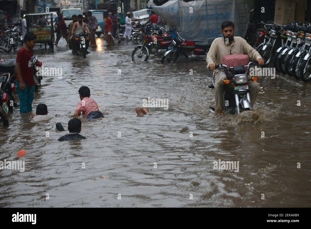 Pakistani commuters wade through a flooded street after heavy monsoon ...