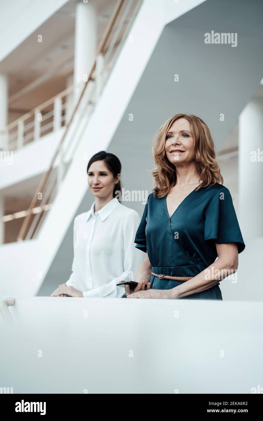 Female colleagues looking away while standing side by side in office corridor Stock Photo