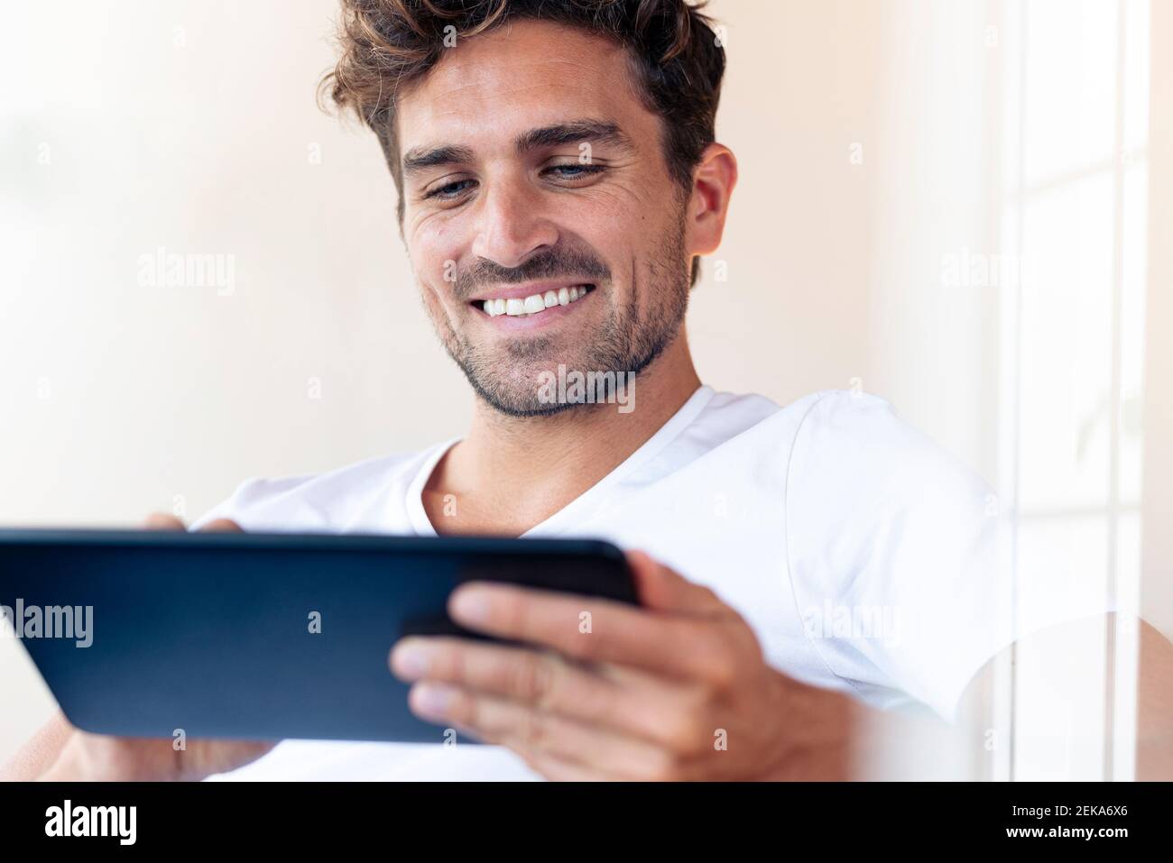 Mid adult man smiling while using digital tablet at home Stock Photo