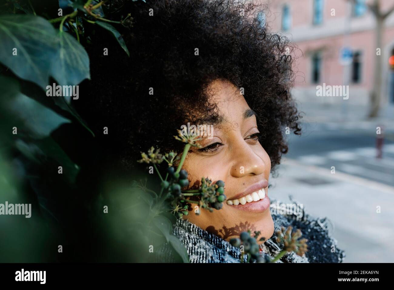 Smiling woman contemplating while leaning on green leaf Stock Photo