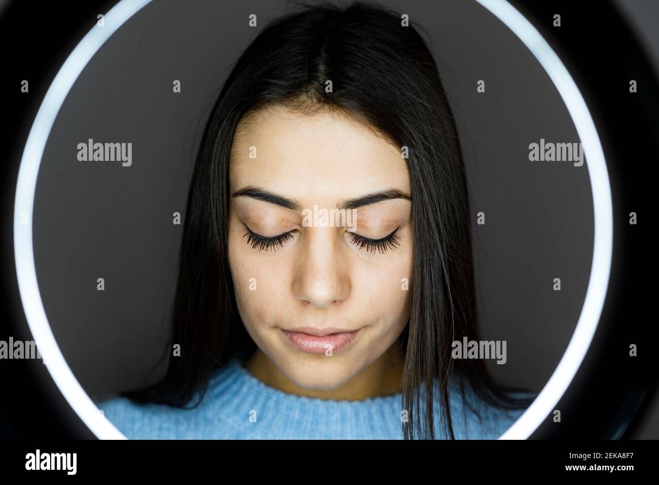 Young woman standing with eyes closed in front of illuminated camera