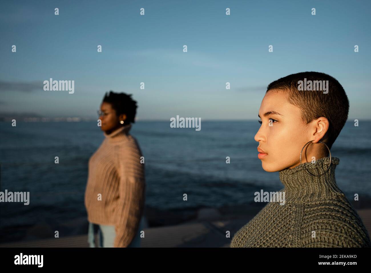 Friends looking away while standing at distance against sea Stock Photo