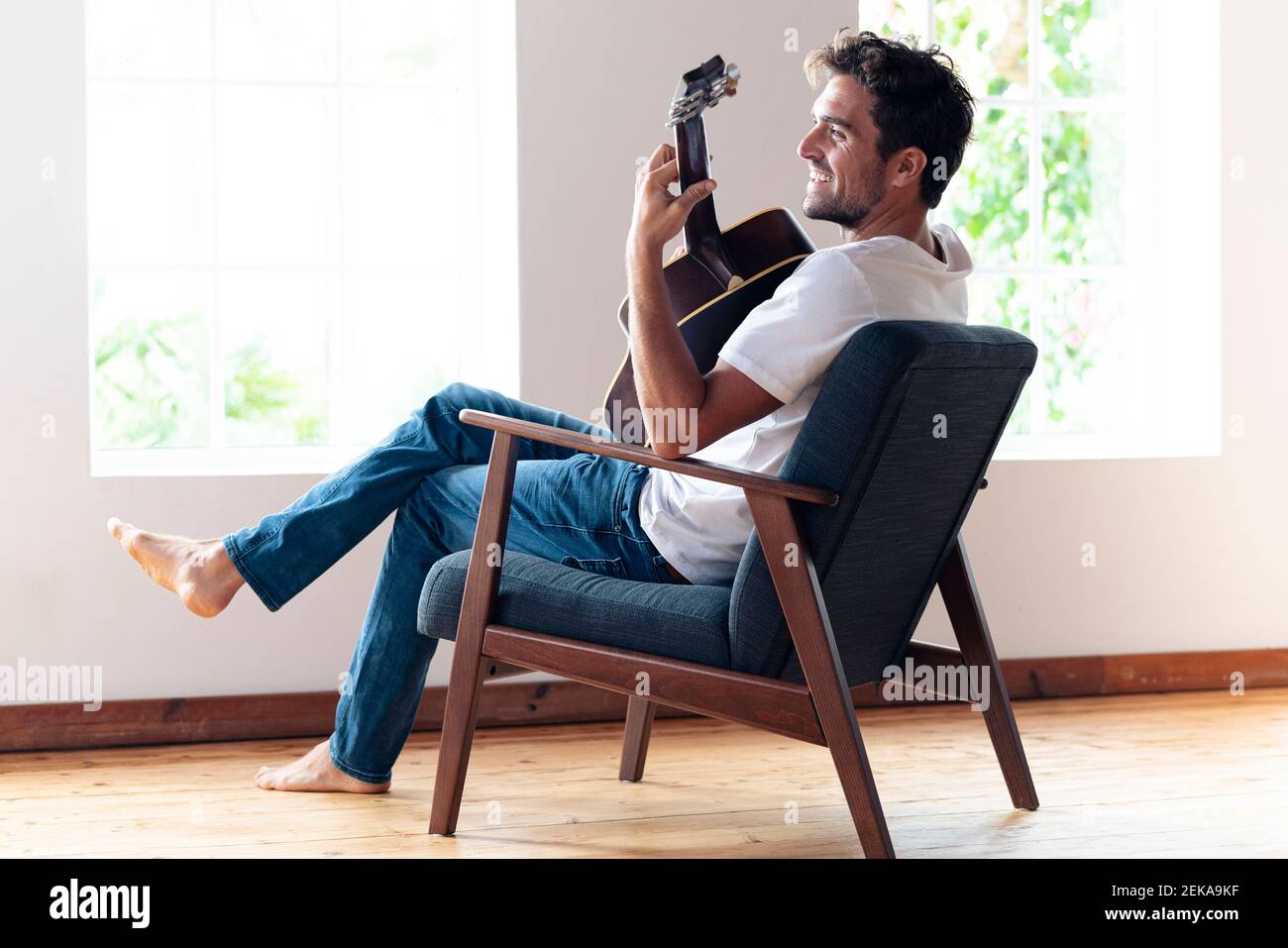 Mid adult man smiling while playing guitar at home Stock Photo