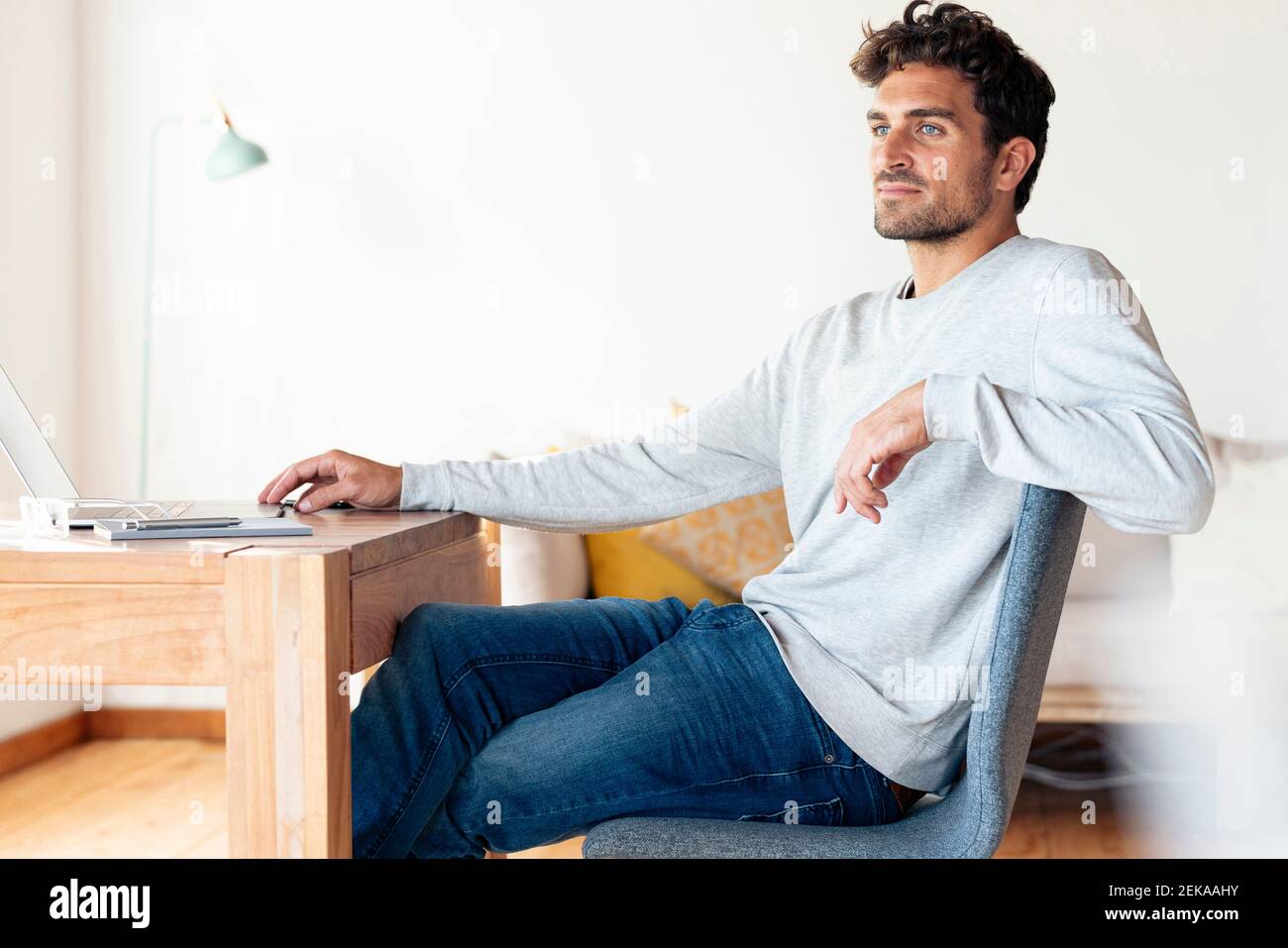 Man looking away while sitting by table at home office Stock Photo