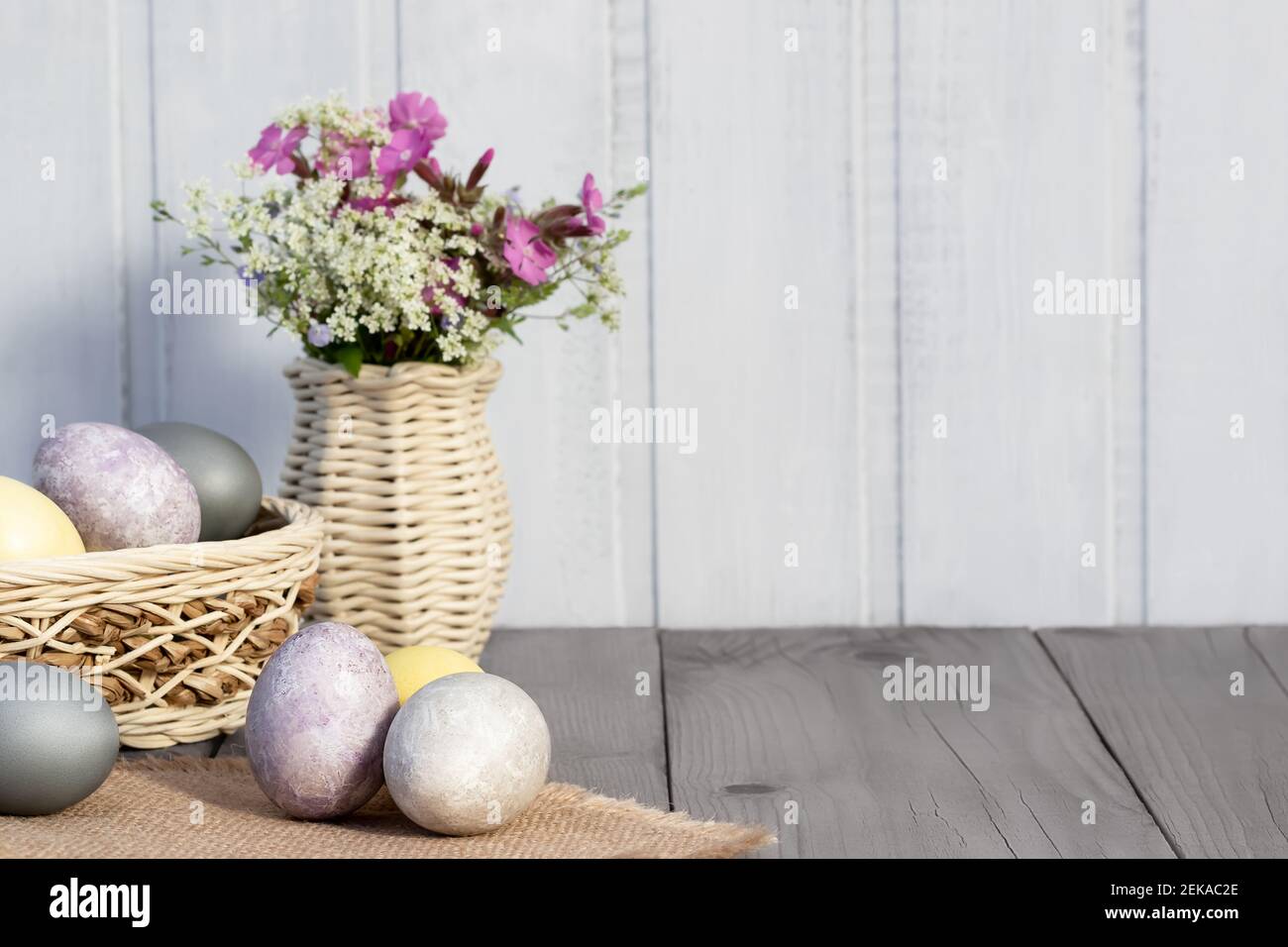 Easter composition - several eggs painted with natural dyes and wildflowers in a vase. Stock Photo
