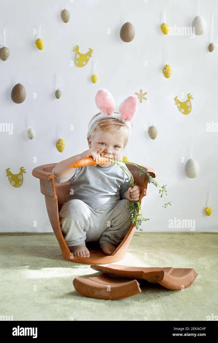 Cute young toddler boy in rabbit ears chewing on a carrot Easter traditions Stock Photo