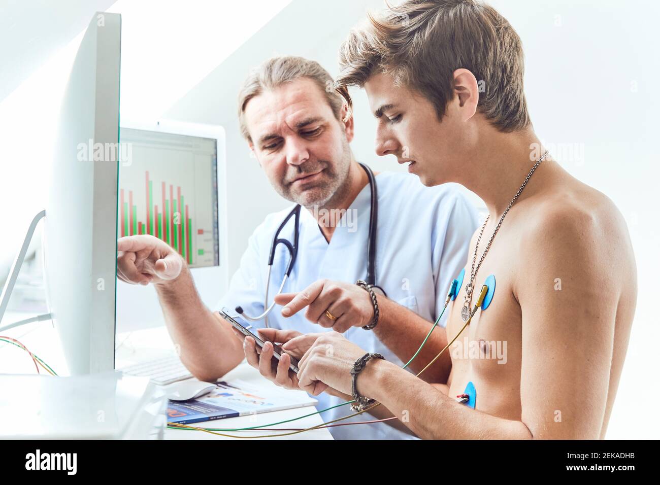 Doctor Explaining To Male Shirtless Patient With Electrodes On Chest 