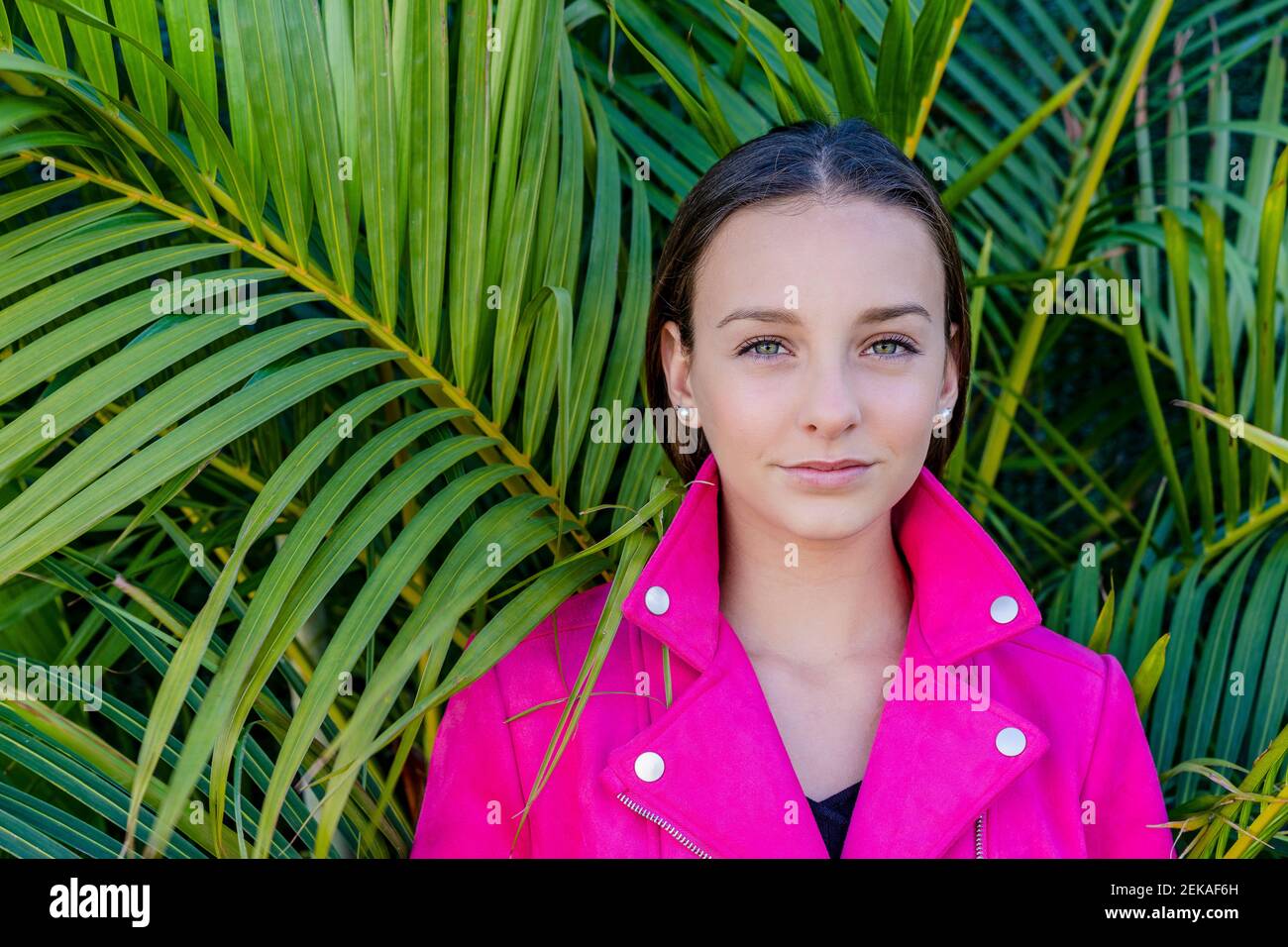 Closeup of teenage girl wearing pink coat against plants in yard Stock
