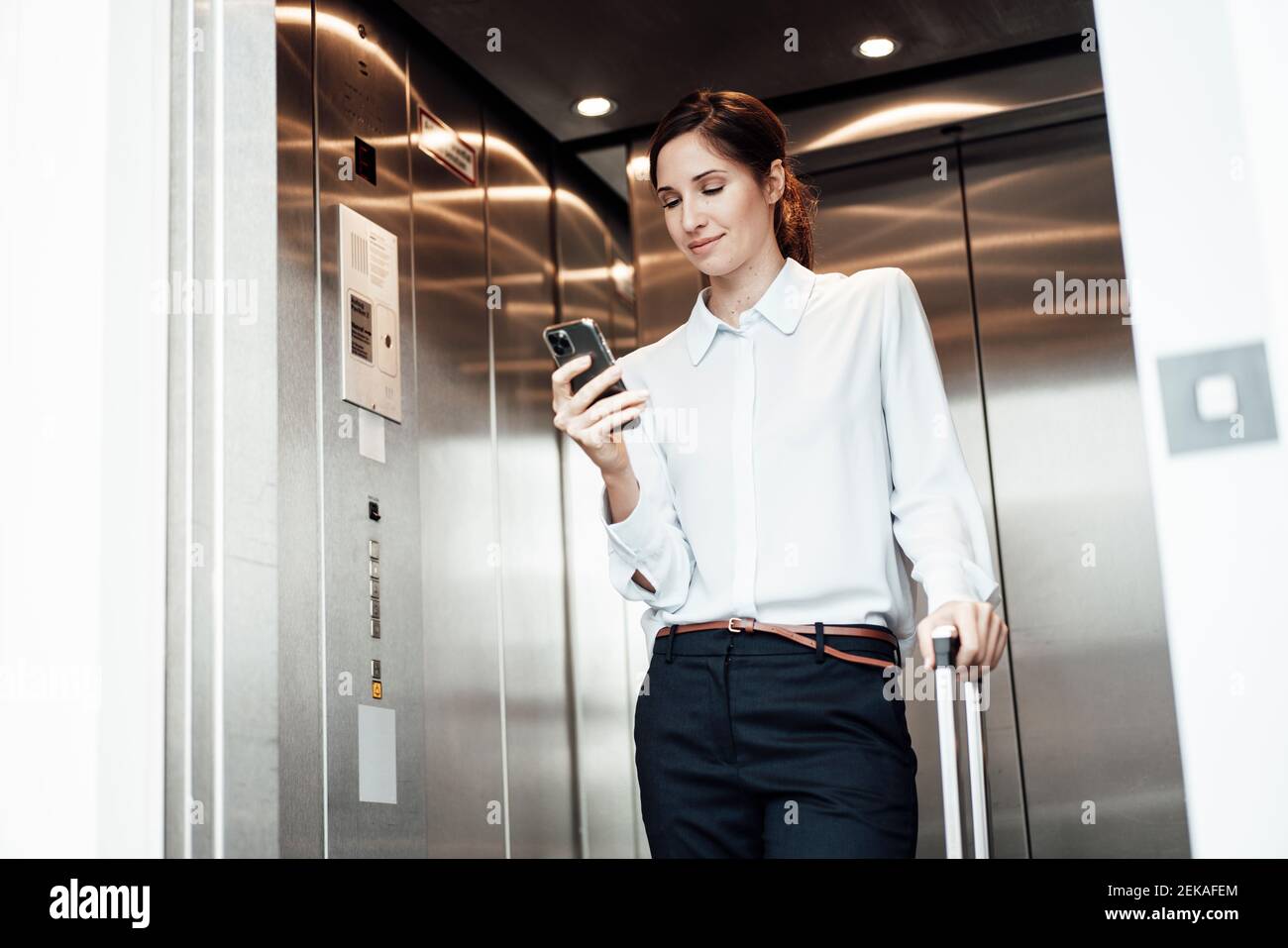 Businesswoman text messaging on mobile phone while standing in elevator Stock Photo