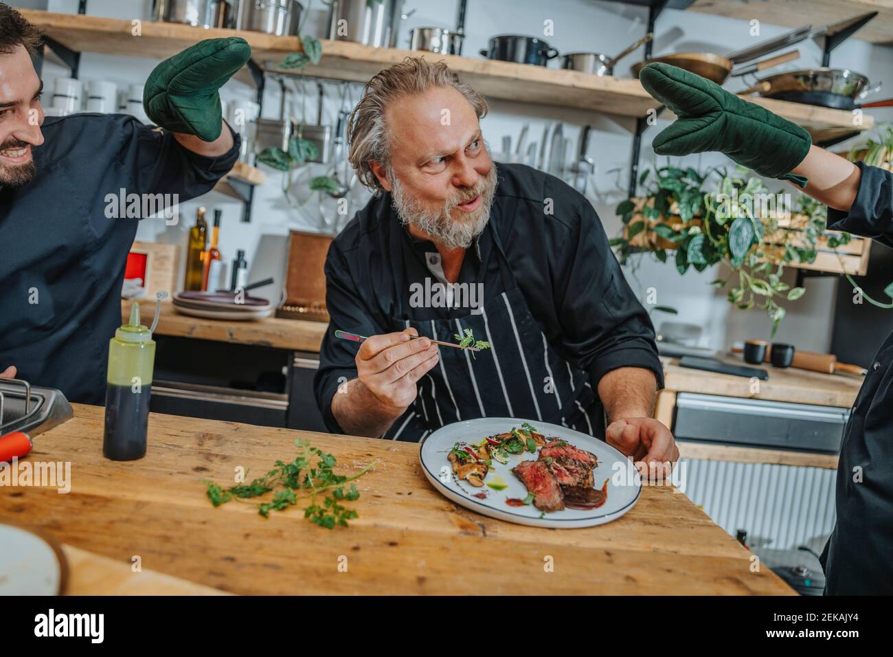 Happy chef looking at colleagues distracting him while working in kitchen Stock Photo