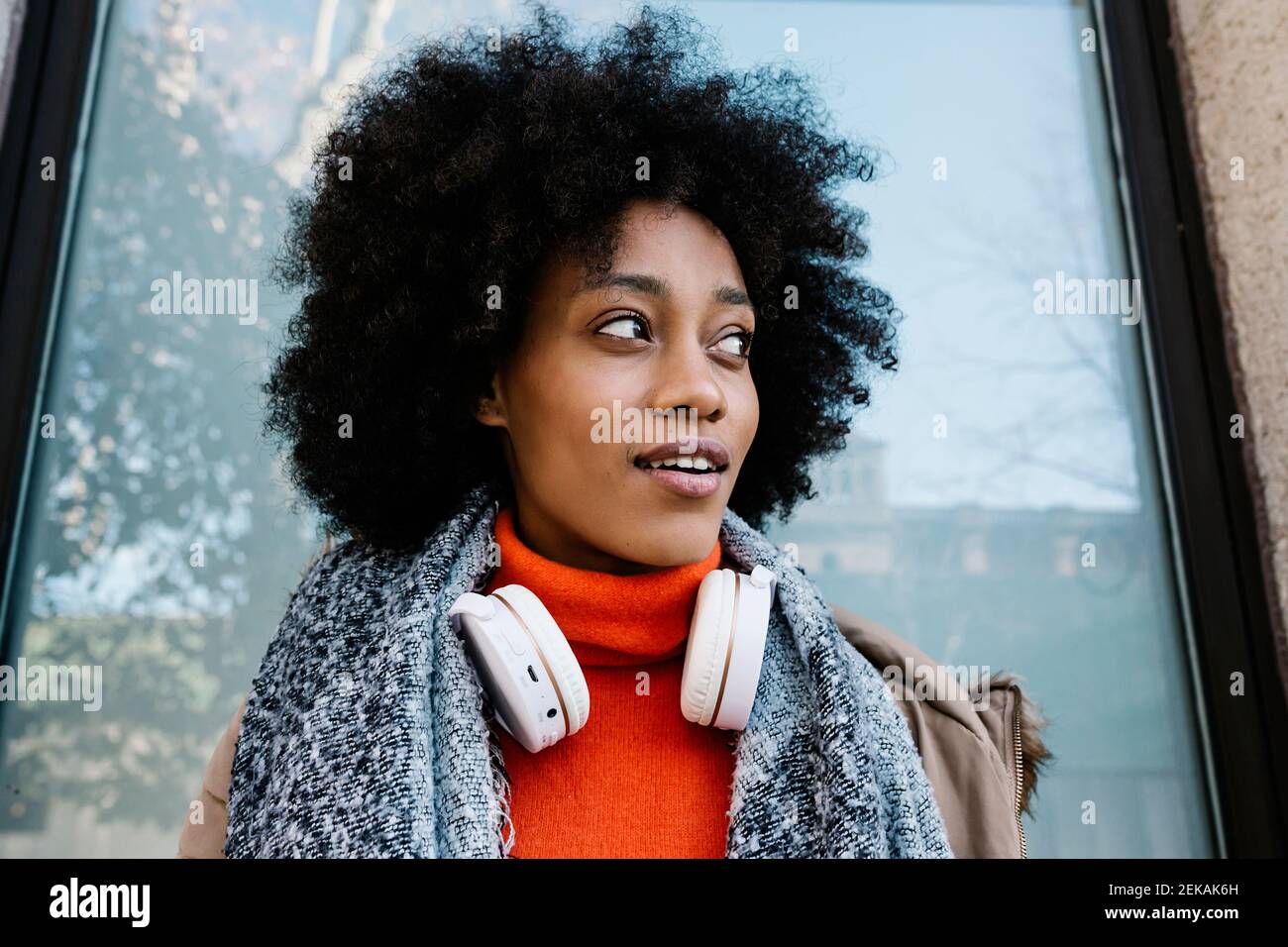 Afro woman with headphones contemplating against glass wall Stock Photo