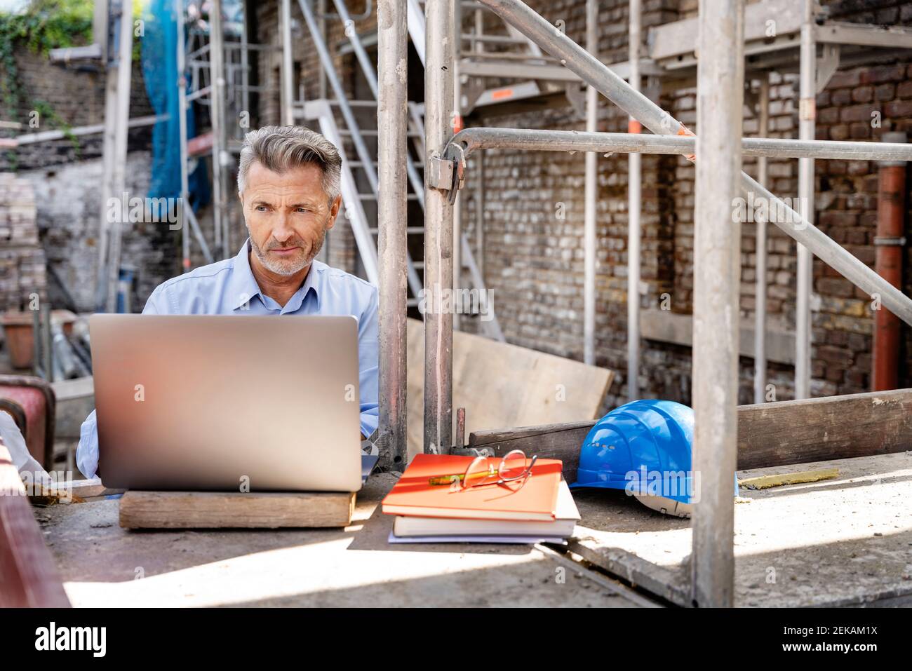 Mature engineer working on laptop while sitting at construction site Stock Photo