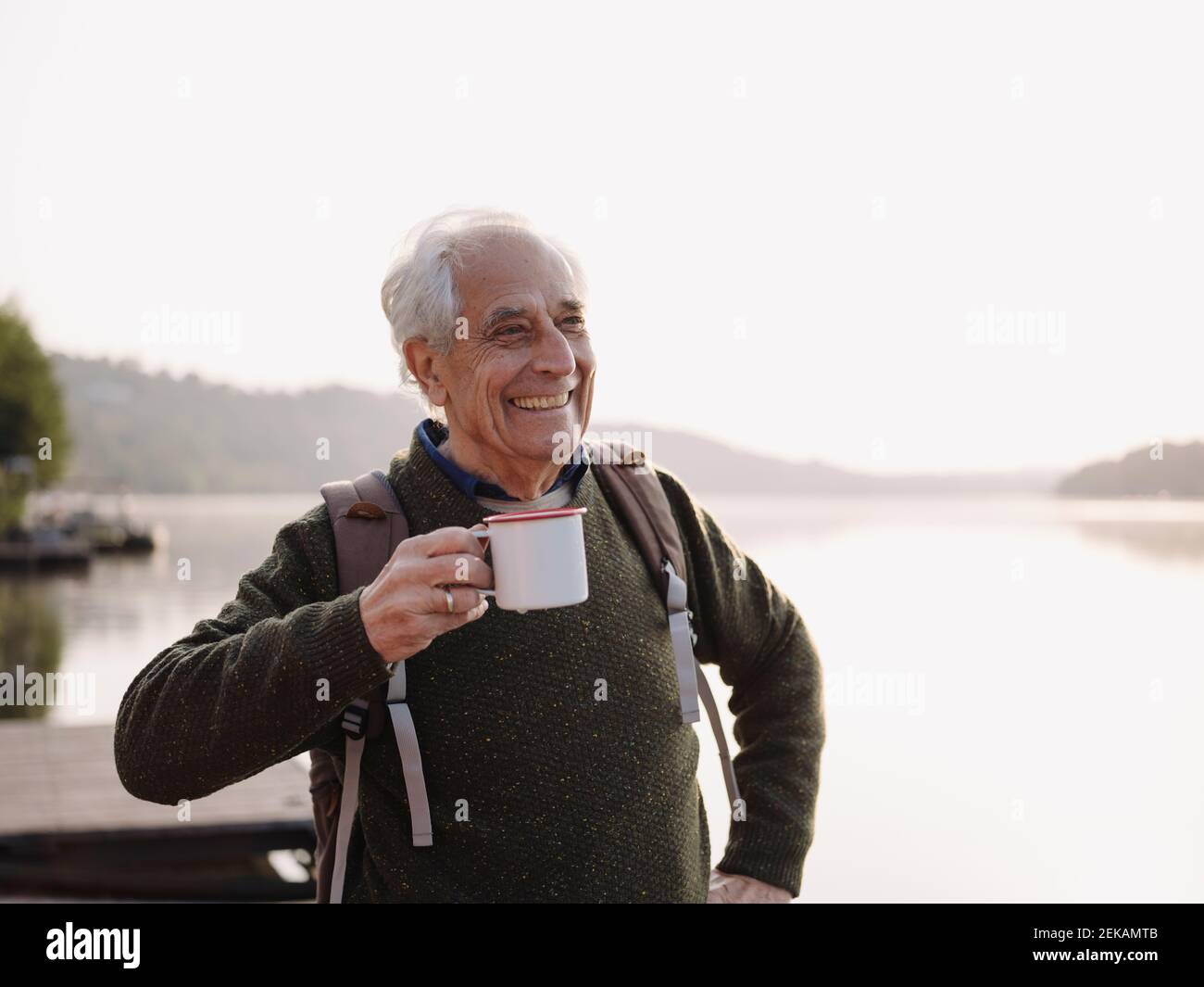 Smiling man with backpack drinking coffee while standing against sky Stock Photo
