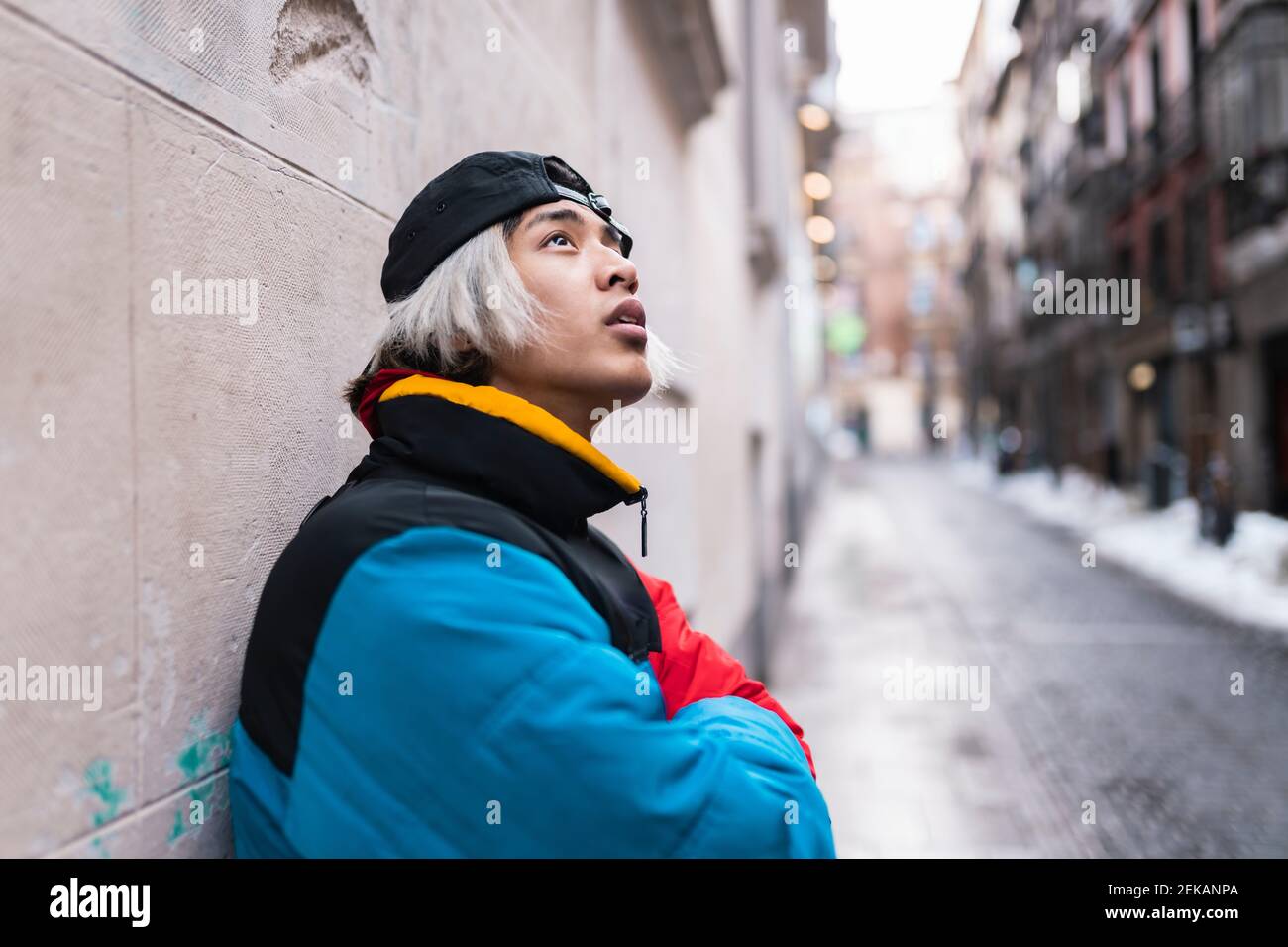 Thoughtful male hipster looking up against wall in city during winter Stock Photo