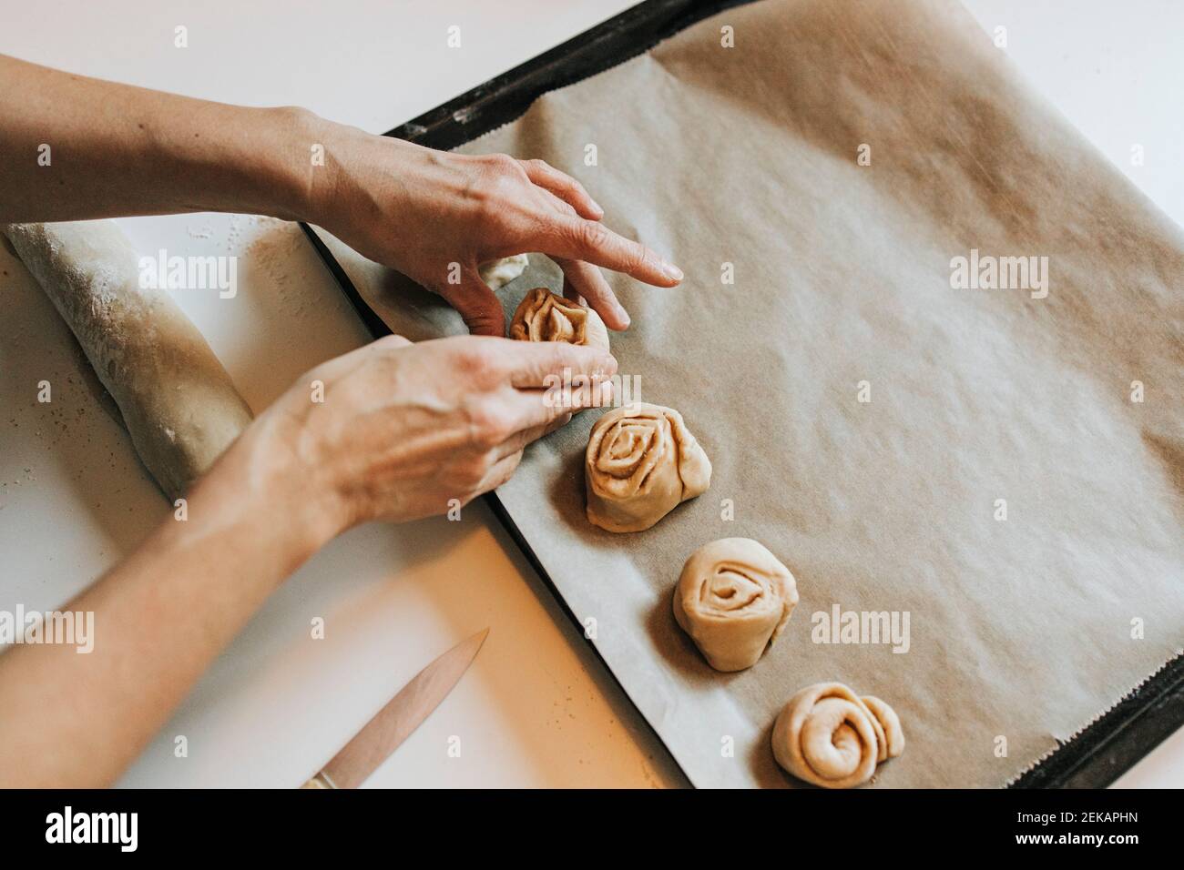 Woman arranging cinnamon rolls on baking sheet Stock Photo