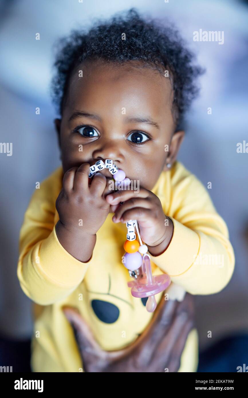 Baby girl chewing toy while held by man Stock Photo