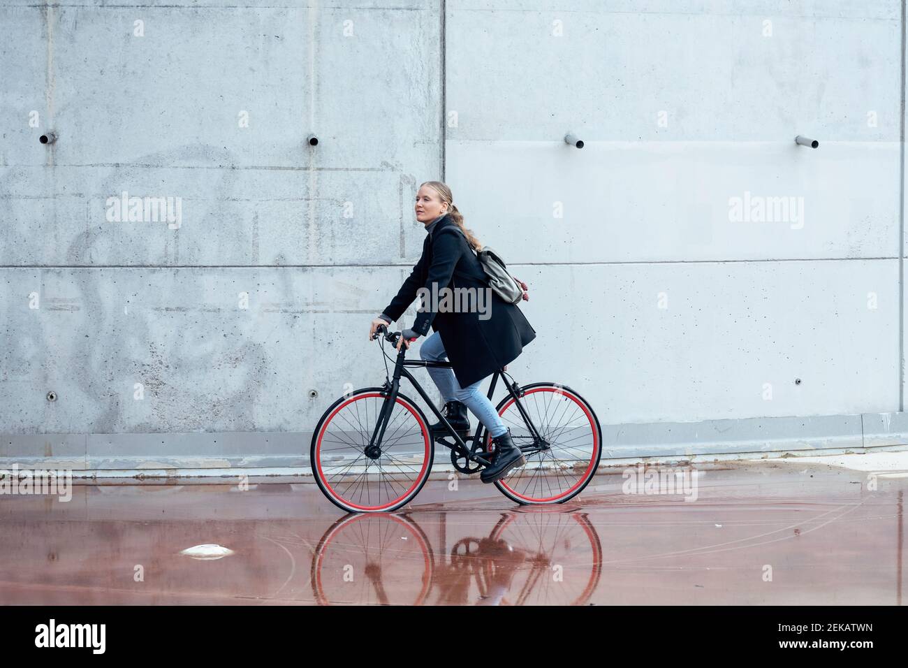 Woman doing cycling on wet road by wall Stock Photo
