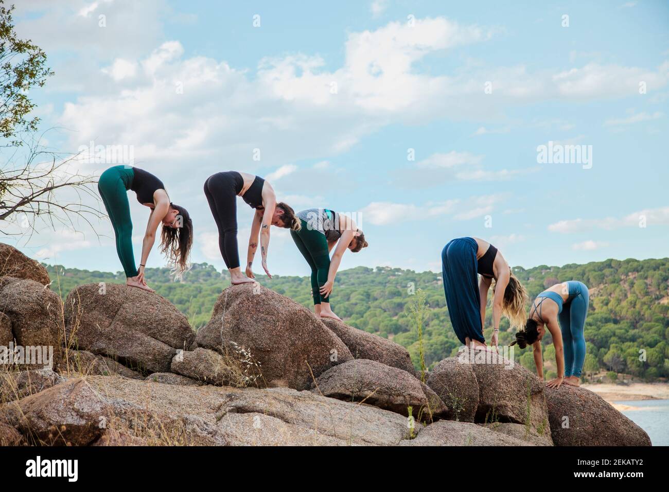 Young women with instructor practicing Uttanasana yoga on rock Stock Photo