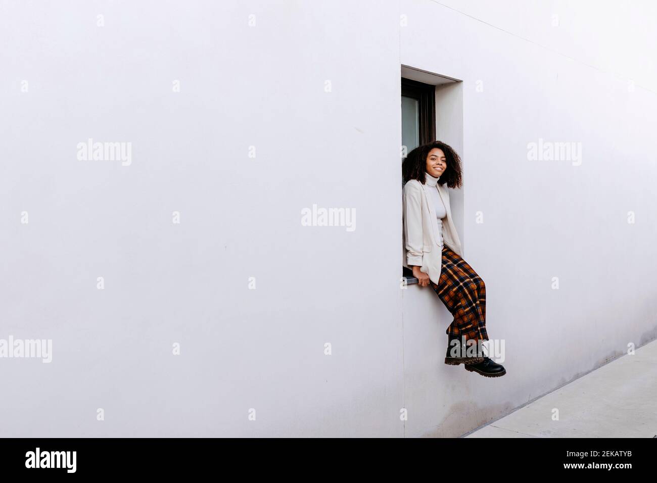 Young woman with afro hair sitting on window sill of building Stock ...