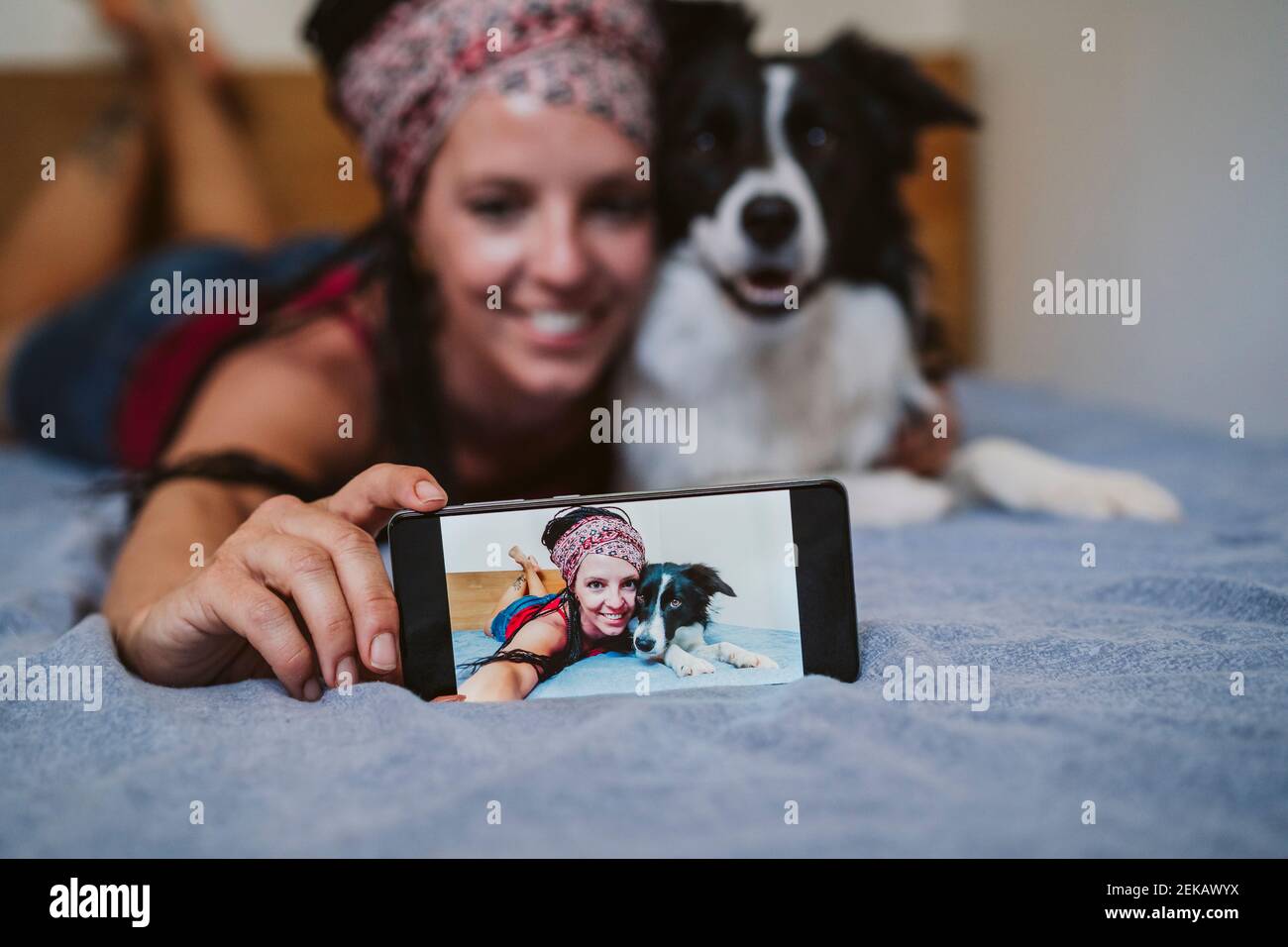 Woman taking selfie through mobile phone while lying on bed with dog at home Stock Photo