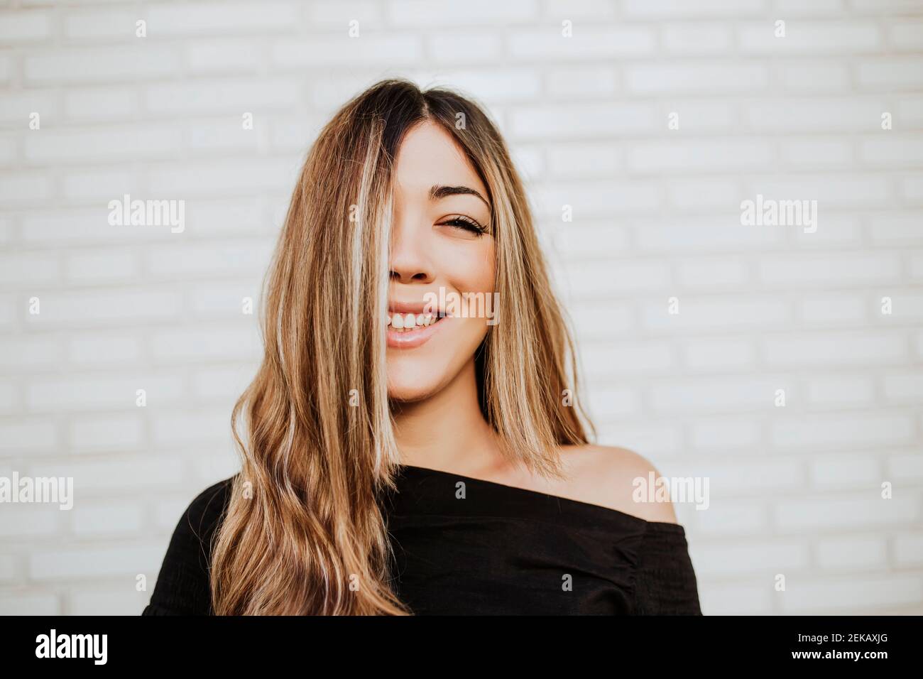 Close-up of smiling young woman covering face with hair against white wall Stock Photo