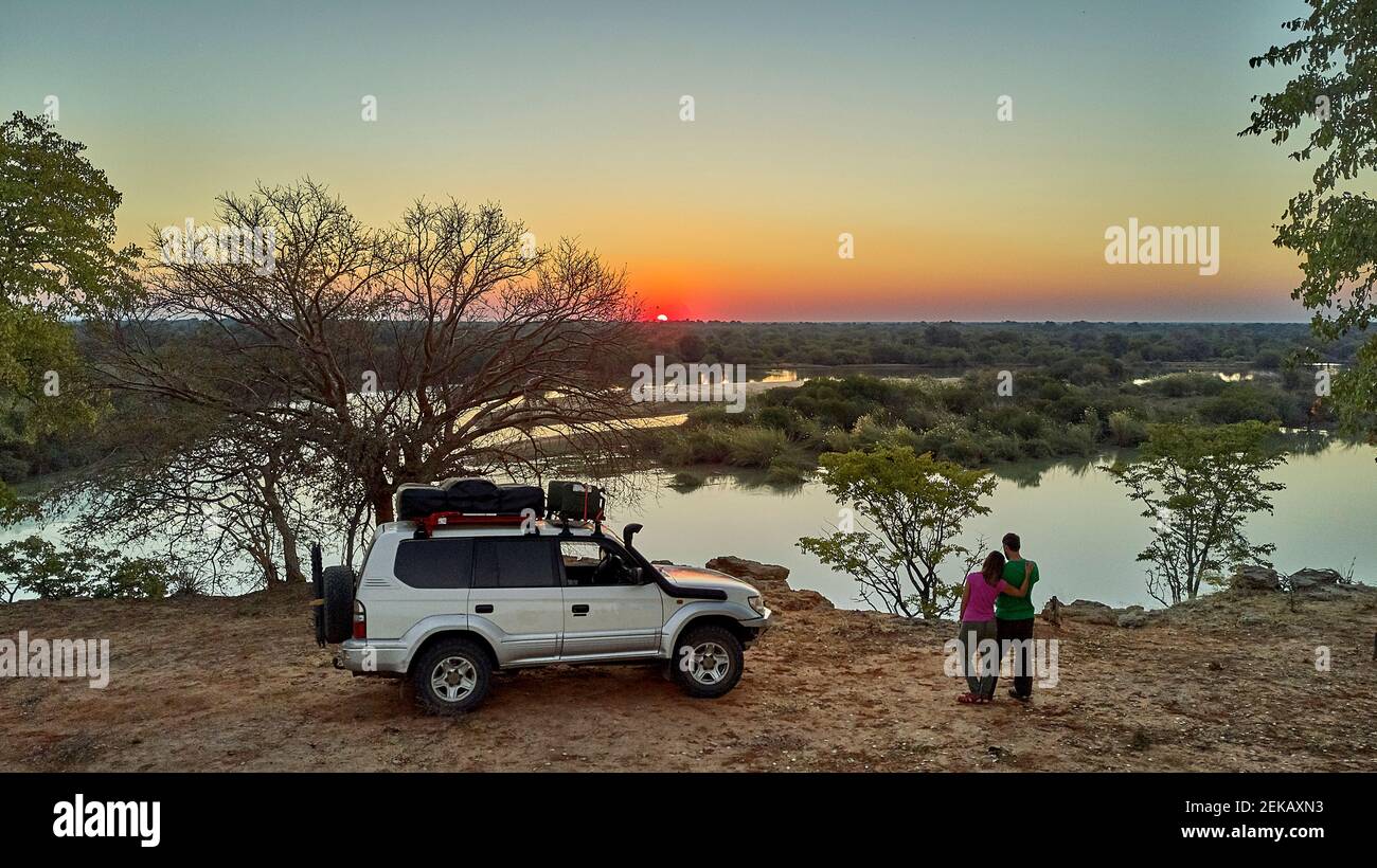 Aerial view of a couple with their jeep enjoying the sunset in front of the river, Cunene river area, Angola Stock Photo