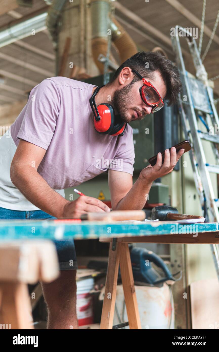 Young male carpenter using smart phone while working in workshop Stock Photo