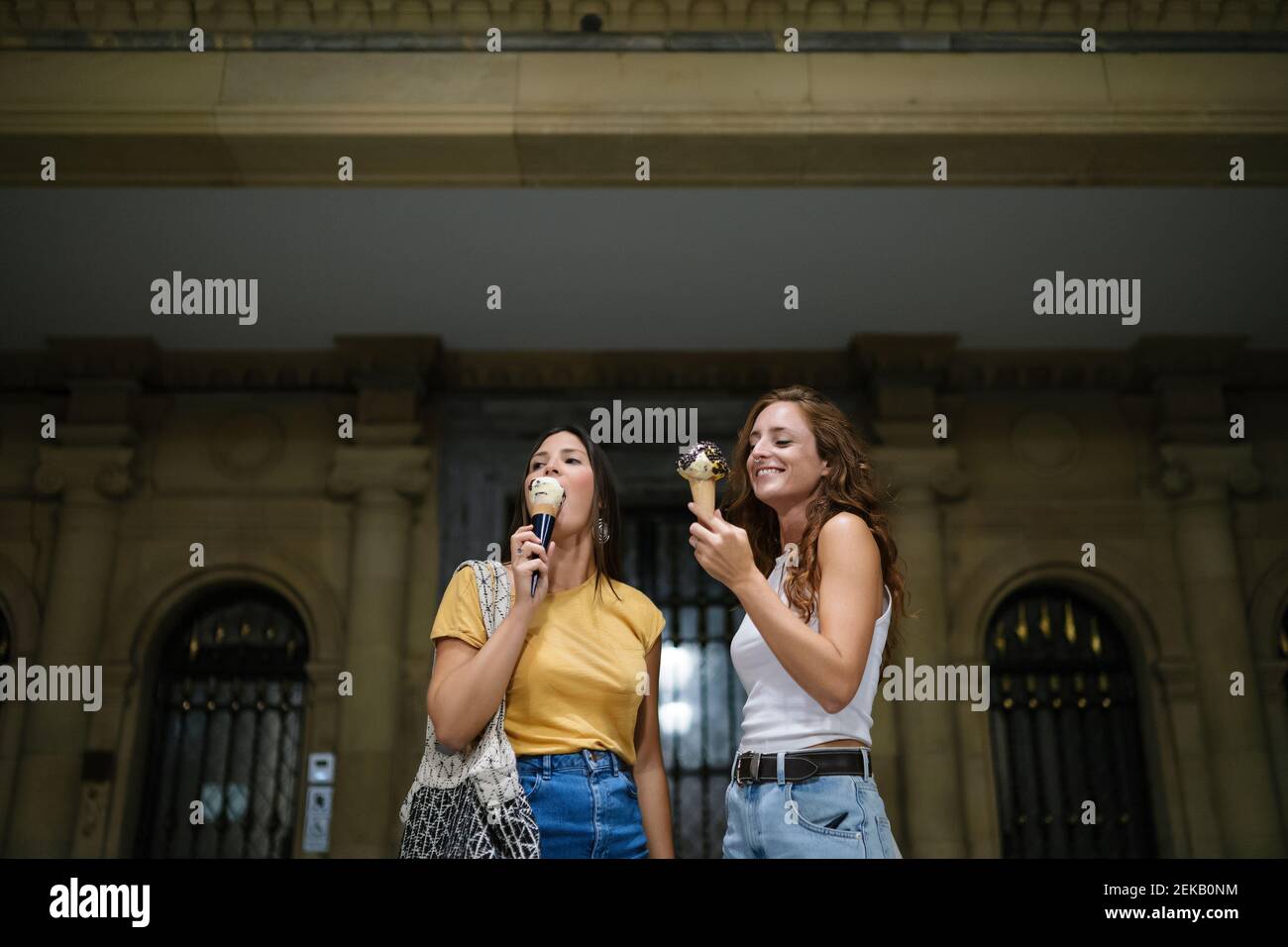 Young women eating ice cream while standing against building Stock Photo