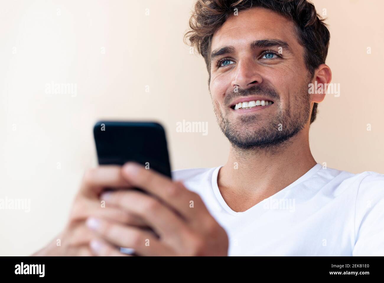 Handsome man smiling while using smart phone at home Stock Photo