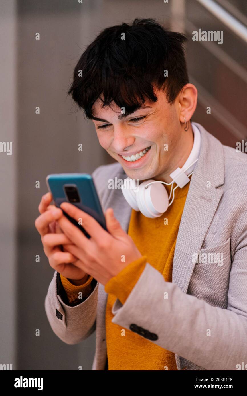 Young man smiling while using mobile phone standing outdoors Stock Photo