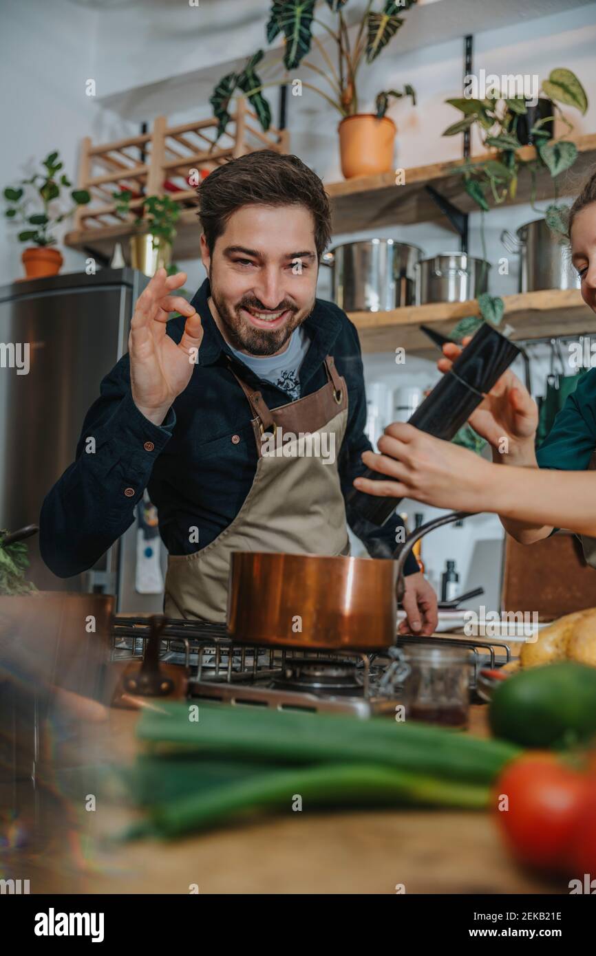 Smiling chef gesturing OK sign while standing by colleague cooking in ...