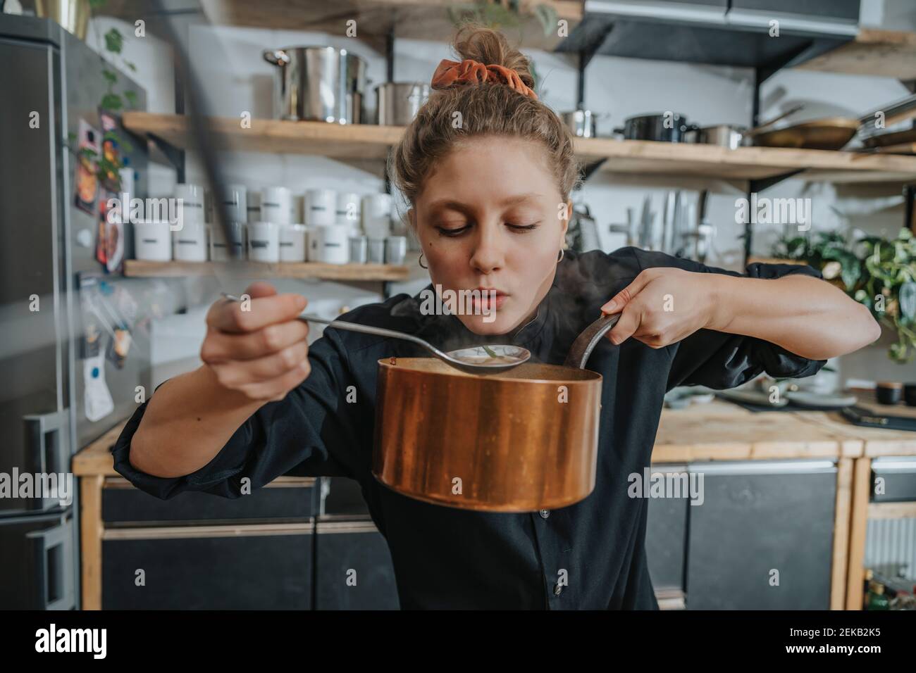 Young female chef tasting Broth soup while standing in kitchen Stock Photo